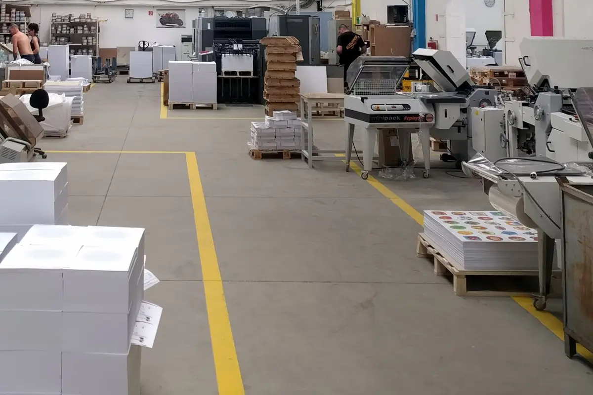 Print production floor with finishing machines, stacked paper and pallets of printed orders