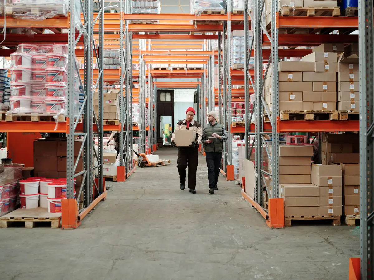 Fulfilment staff walking a long racked warehouse aisle stocked with boxed orders